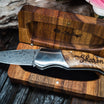 A folding knife with a birch wood burled handle and an intricately etched blade